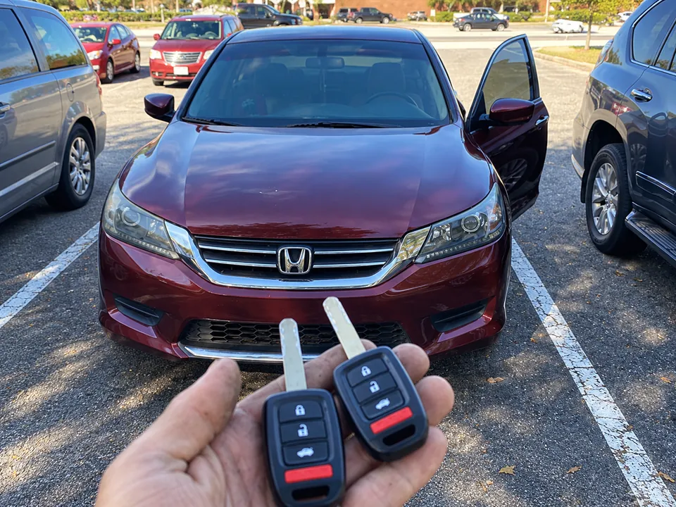 Two Honda remote keys held in front of a burgundy Honda car